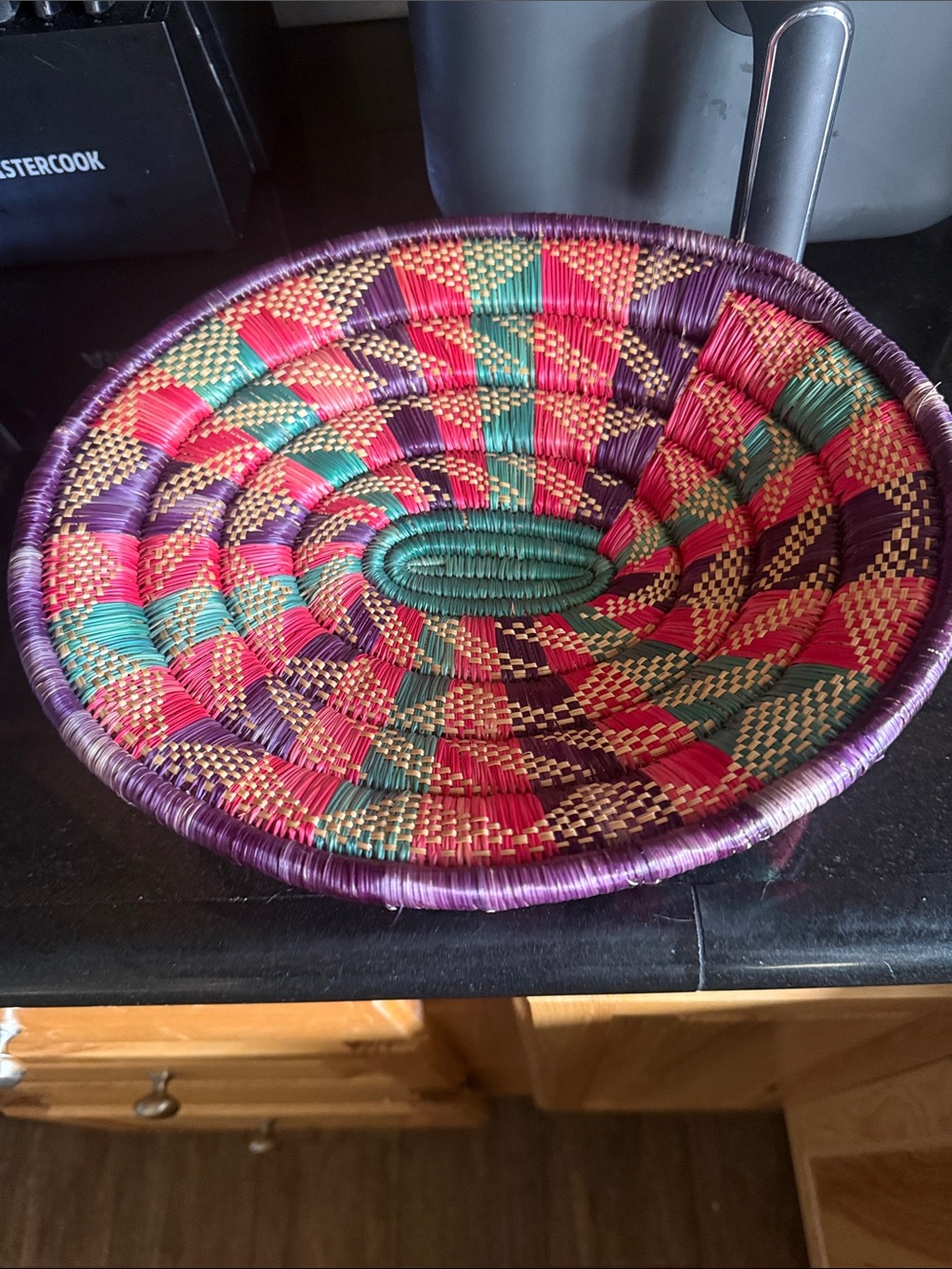 An oval East African coiled basket with colorful geometric patterns.